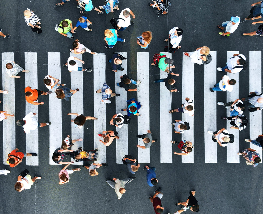 Aerial view of people crossing a busy street at a crosswalk, representing urban life and daily commute.