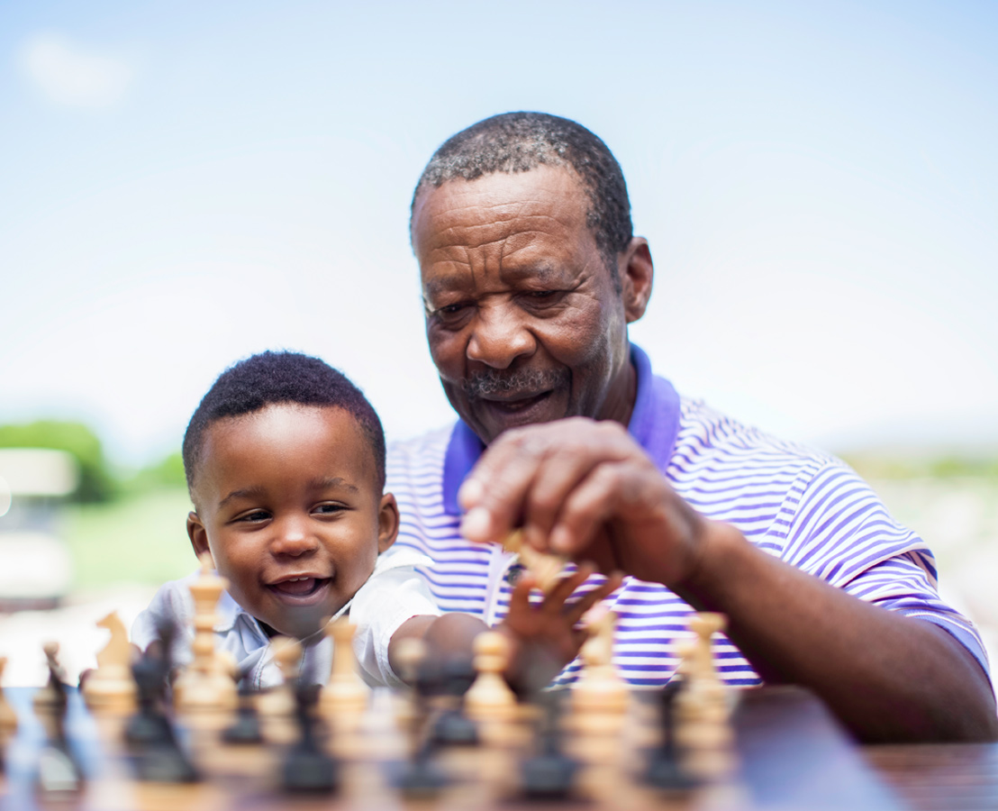 Grandfather and young grandson playing chess outdoors, representing bonding and intergenerational learning.