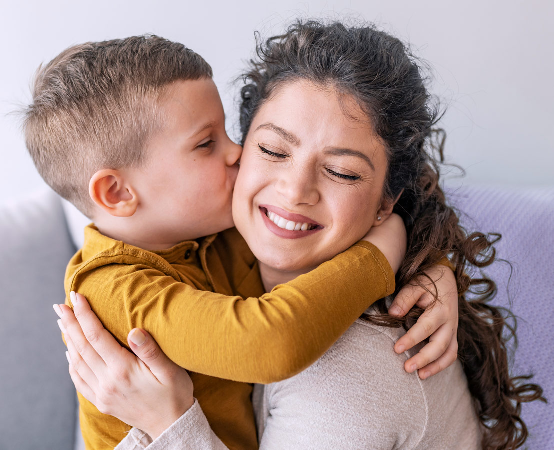 Young boy kissing his smiling mother on the cheek, depicting a loving and affectionate family moment.