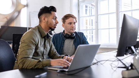 Two young professionals collaborating on a project at a computer, representing teamwork and modern office work.