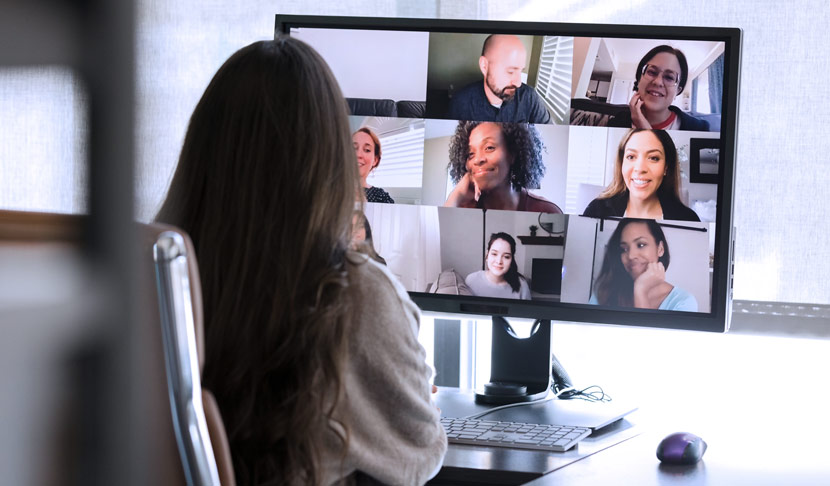 Person participating in a virtual meeting with multiple colleagues on a computer screen, representing remote work and online collaboration.