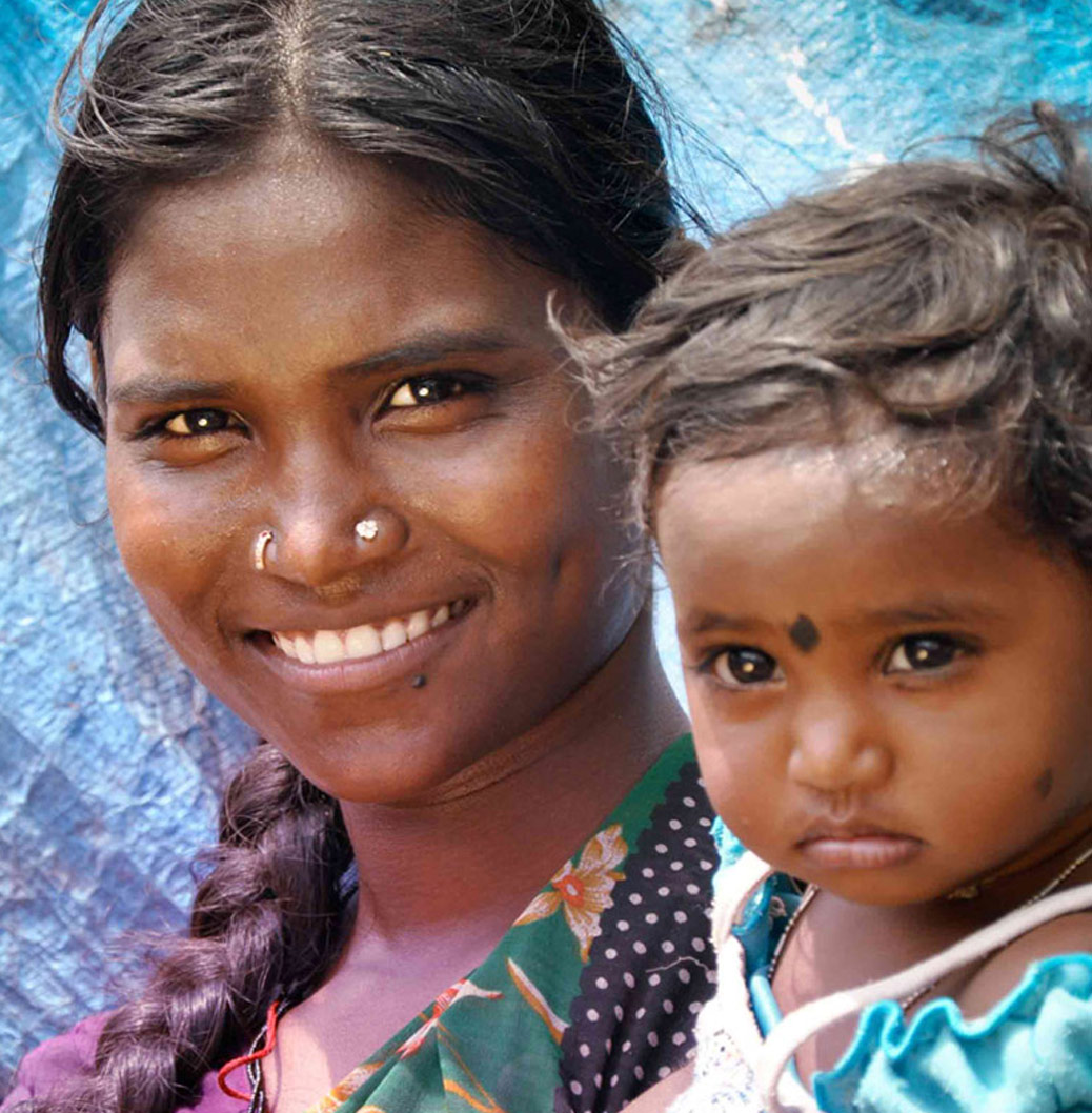 Smiling mother with braided hair and child in traditional attire against a vibrant background, showing family and heritage.