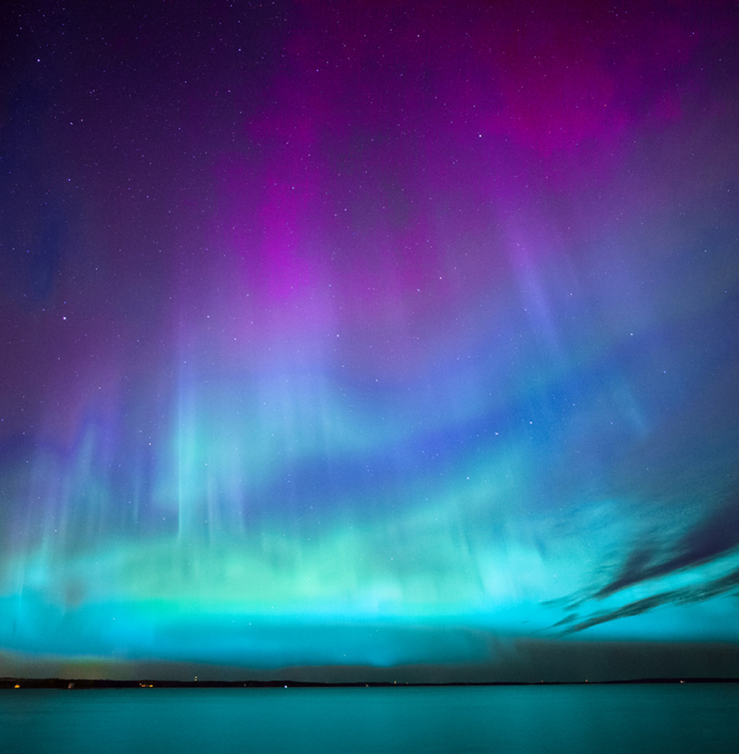 Vibrant northern lights display in the night sky over calm water, showcasing the beauty of natural phenomena. 
