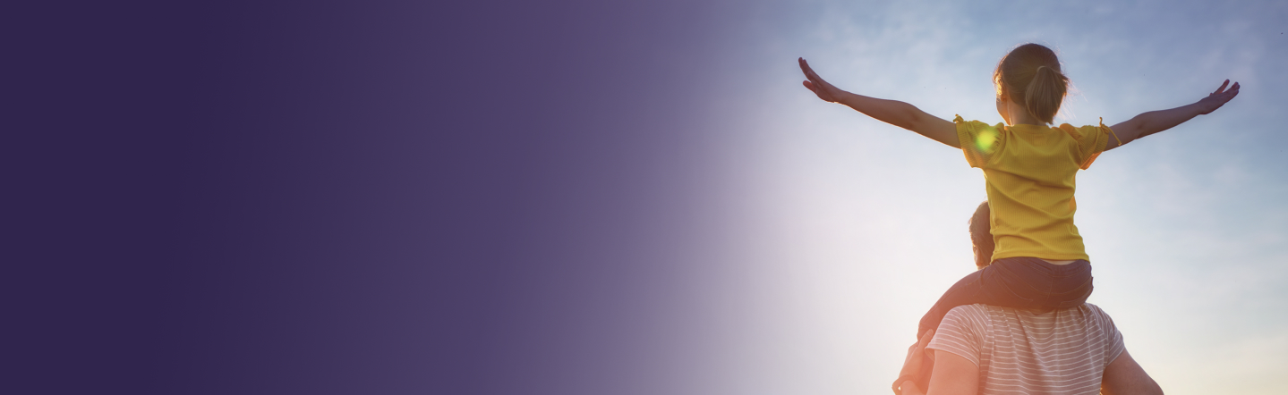 Child in yellow shirt on adult's shoulders, arms outstretched against a bright sky, depicting joyful family bonding.