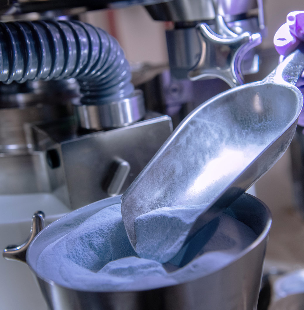 Scientist wearing purple gloves scooping a powdered substance in a lab, representing precision in pharmaceutical manufacturing.